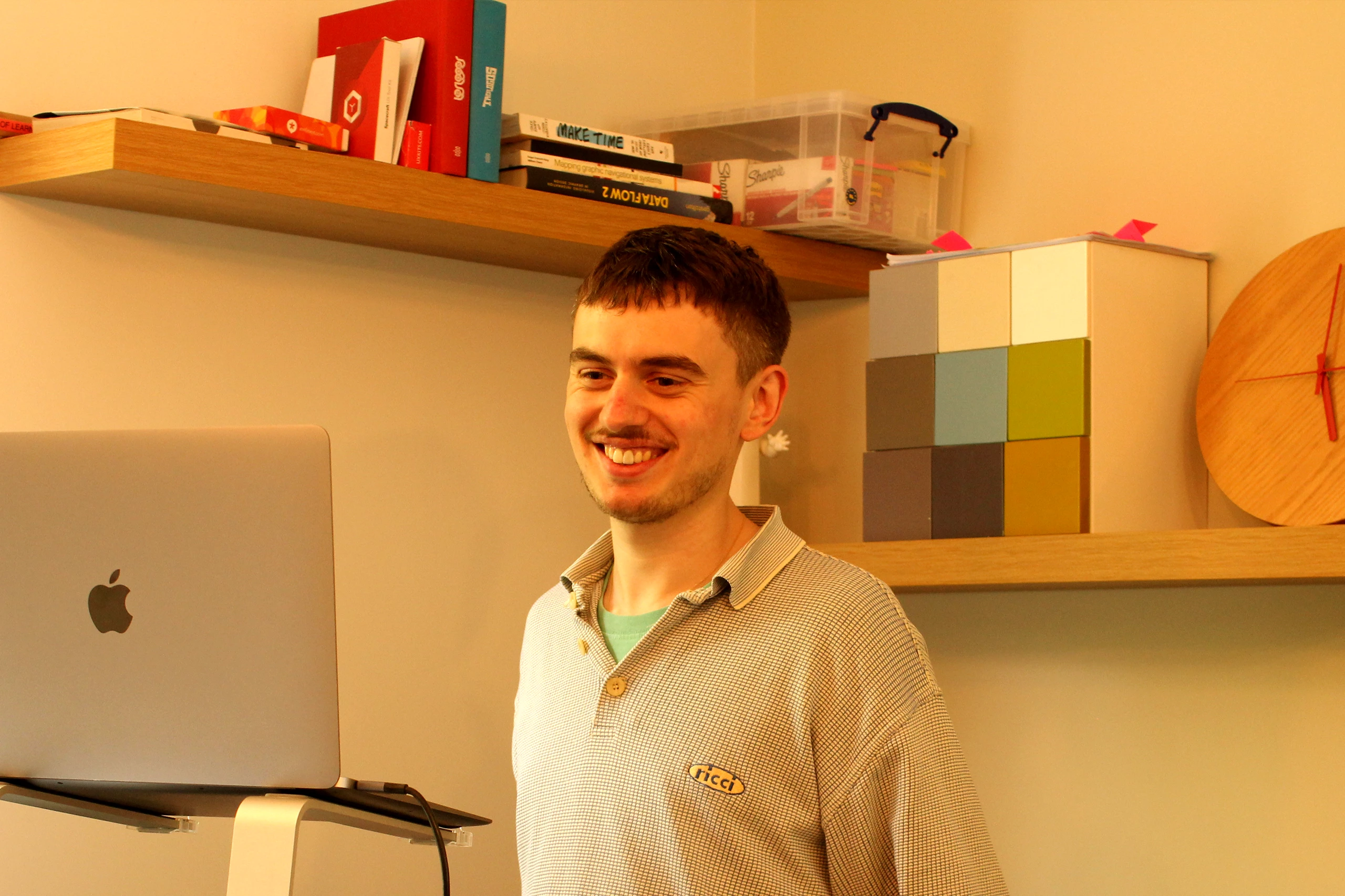 Digital Engagement Manager Dom stood at desk smiling, looking at Macbook screen