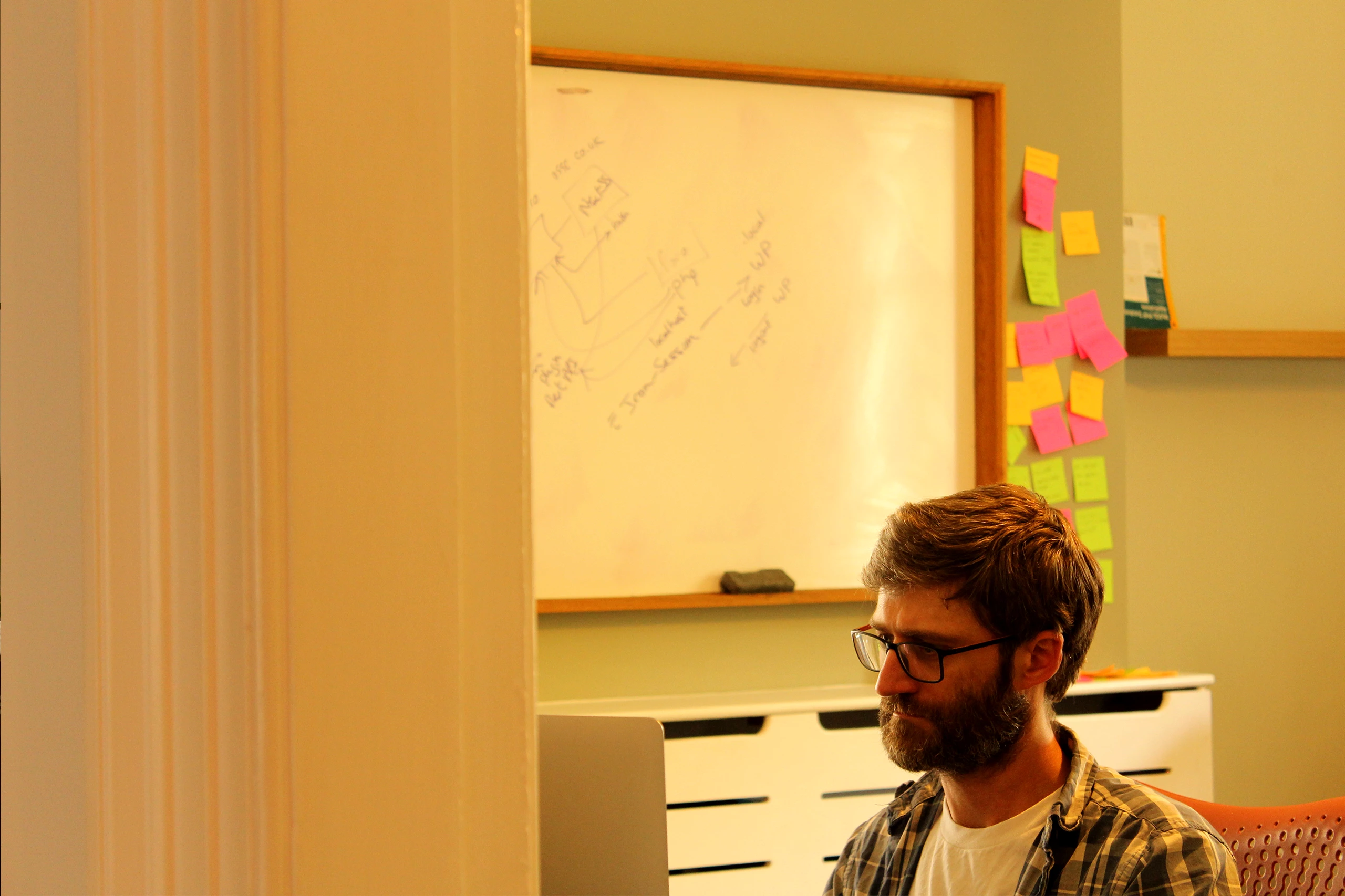 Developer Mike looking at monitor, with whiteboard and post-it notes in the background